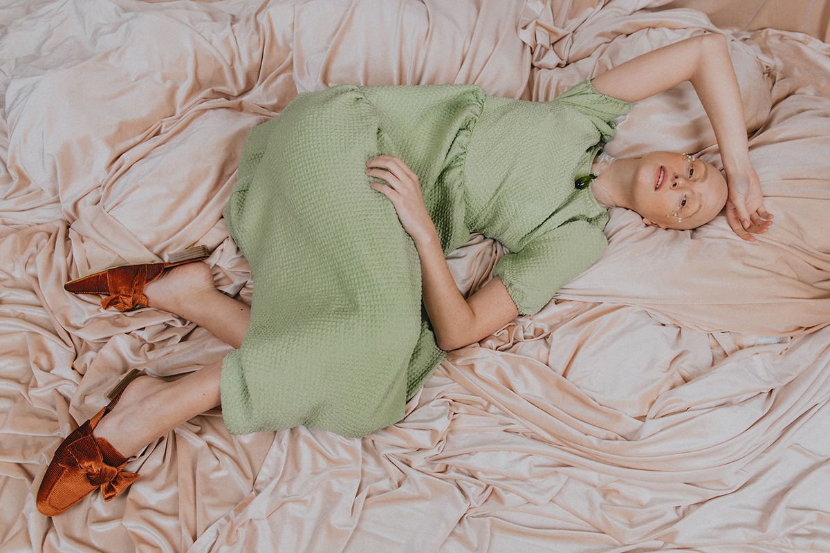Woman laying in bed wearing green dress and red sandals