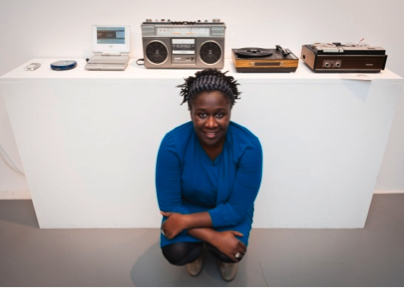 Photo showing artist and curator Barby Asante in front of exhibition display