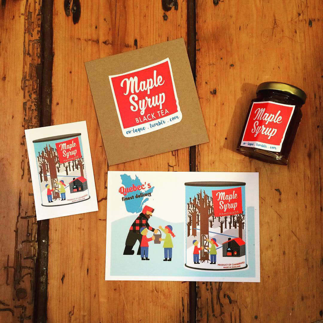 Just some of Eve Laguë's maple syrup products available in her small business. Including illustrated characters tapping maple syrup on a sticker and postcard. A tea bag of Maple Syrup Black Tea and a small jar of maple syrup