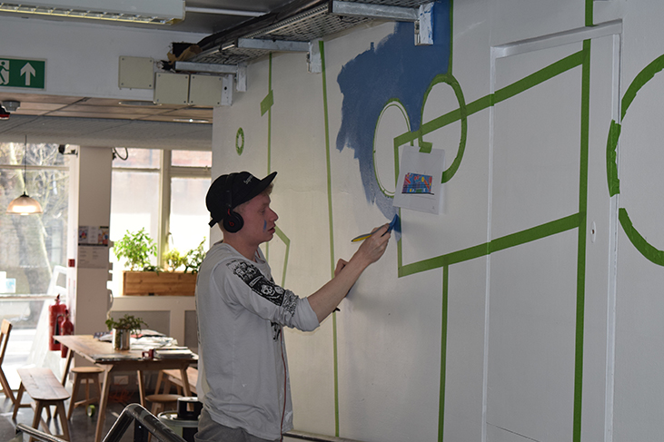 Kyulx begins painting in blue around the green masking tape