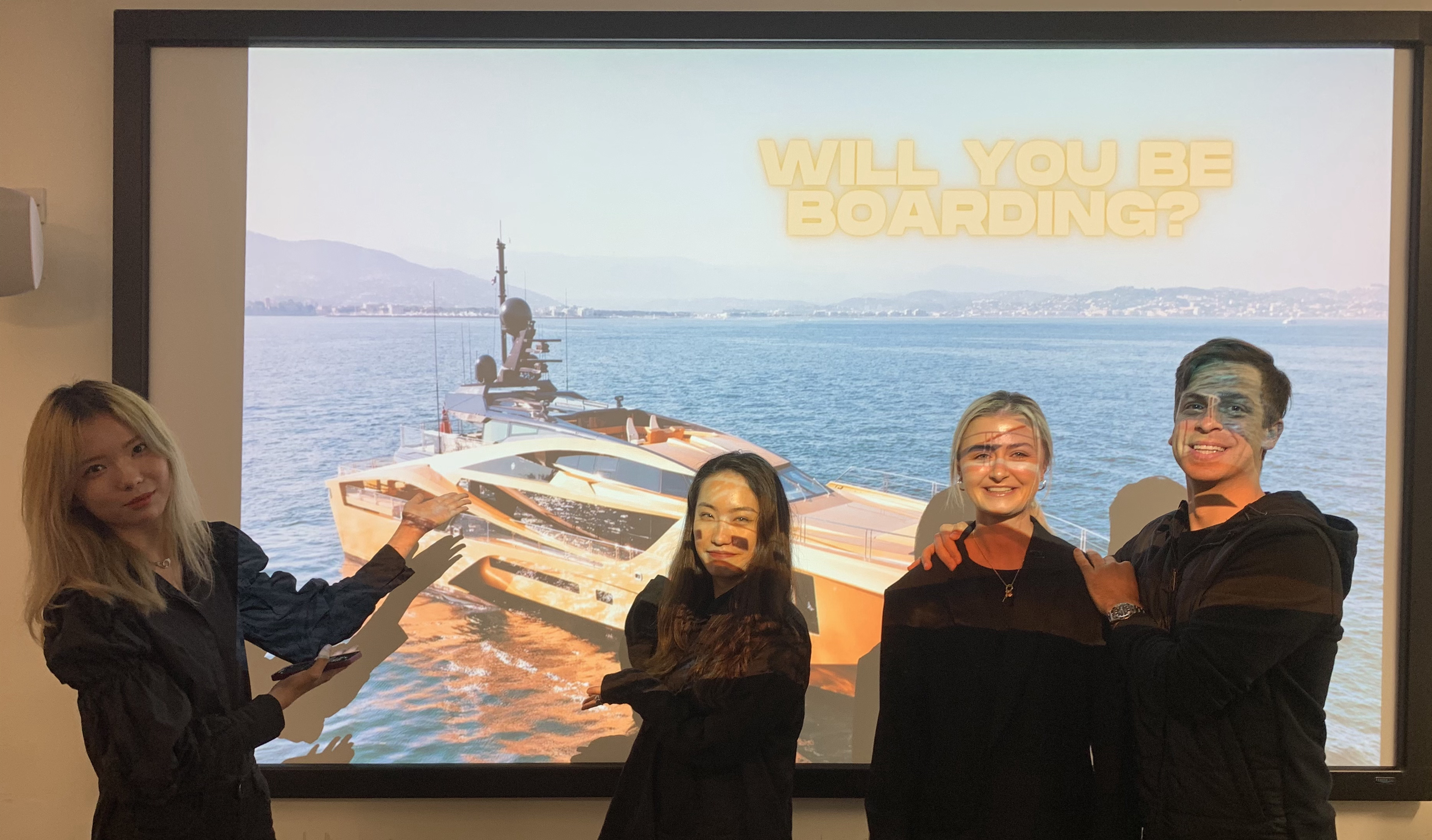 four students posed in front of a projector in a classroom