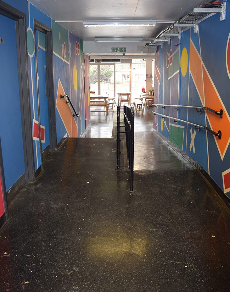Looking down the corridor with either wall fully painted in blues and purples with geometric shapes cutting into the main blocks in red, yellow, green and orange