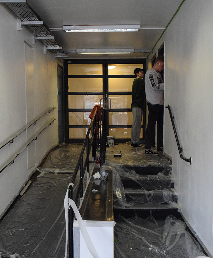 Kyulx and friend standing at the end of the corridor putting the grid for the mural on the right hand side wall