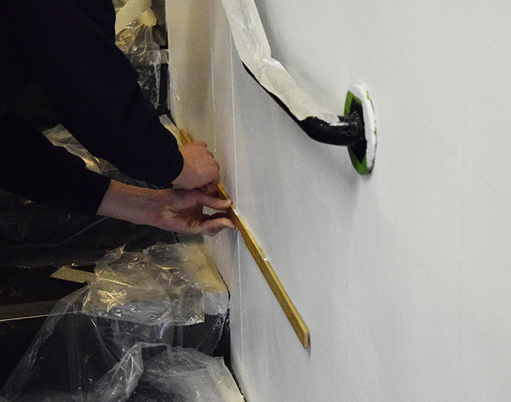 A close up image of a white wall with two hands holding a ruler and a pencil to start ruling out the grid for the wall mural