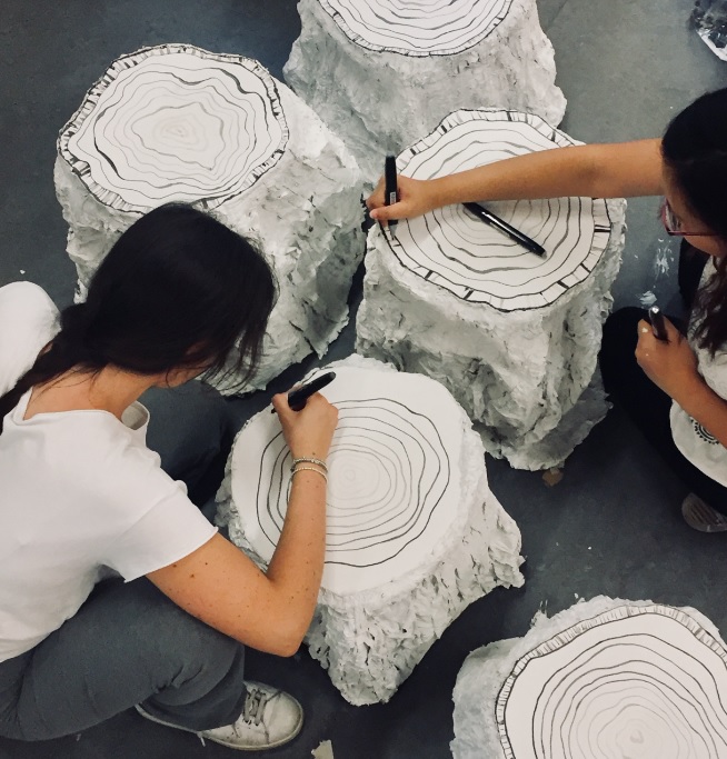 Students drawing rings on the tree stump stools that will be displayed around the campfire