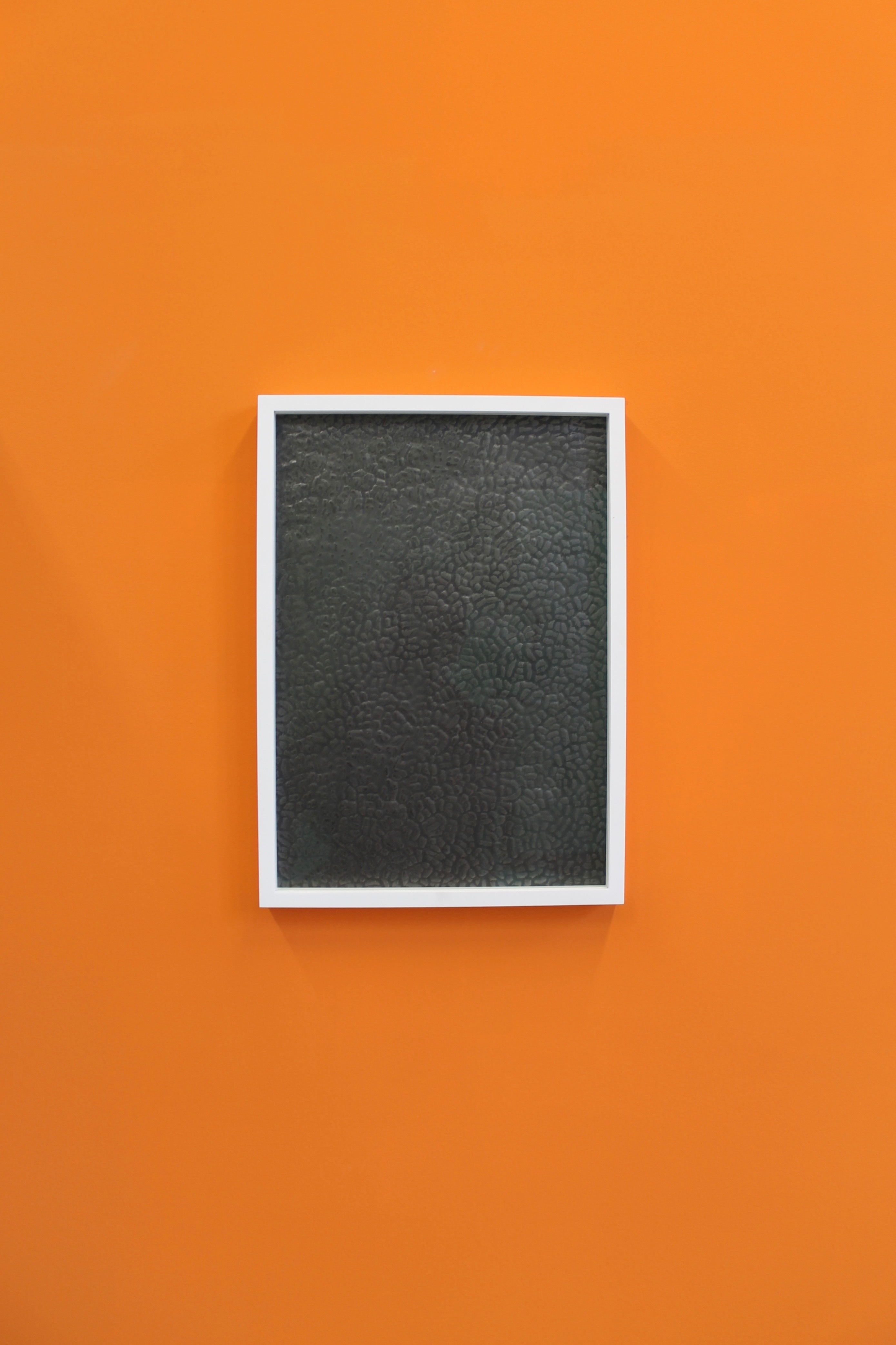John Bingham's "Graphite Window", a graphite textured portrait drawing in a white block frame on a orange painted wall