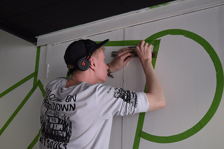 Kyulx placing green masking tape on to the wall to outline the geometric shapes for the wall mural