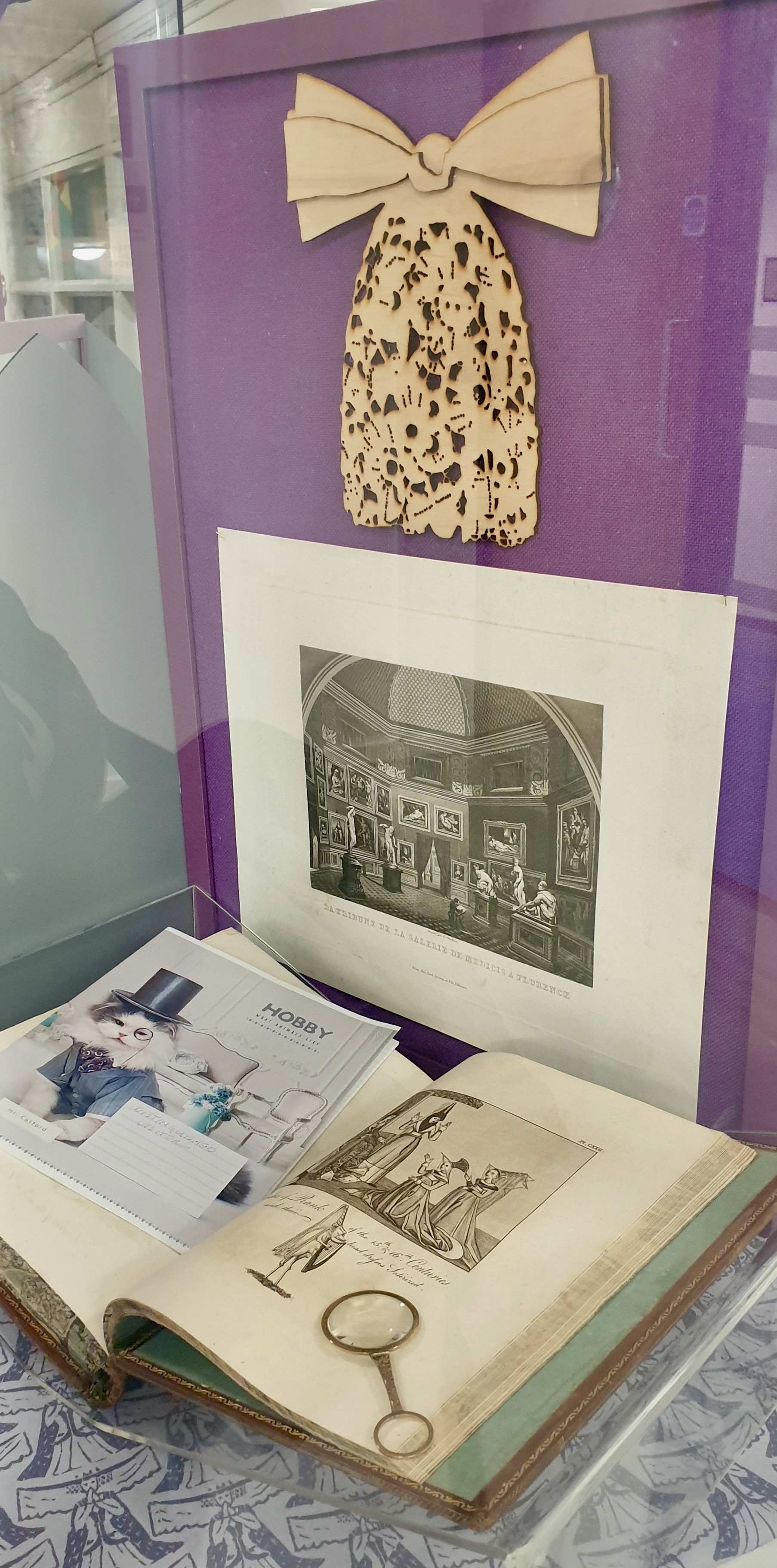 Display of wooden bow, picture and open book against purple background  in display cabinet