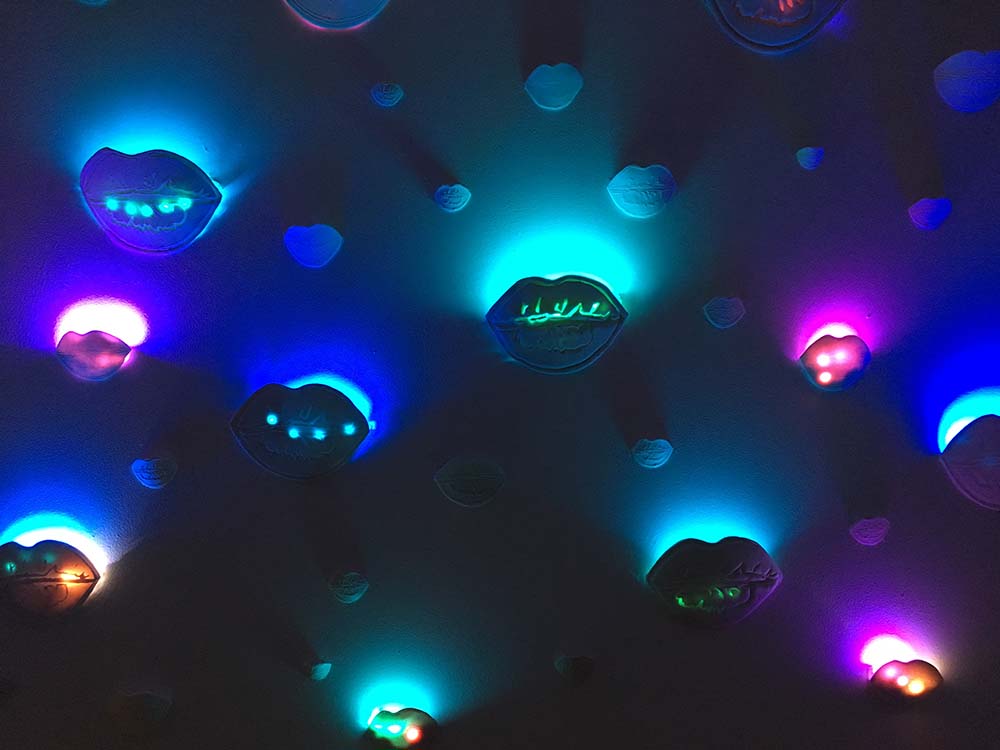 Installation shot of ceramic lips lit with LED lights from We Need to Talk by Sharon Bertram.