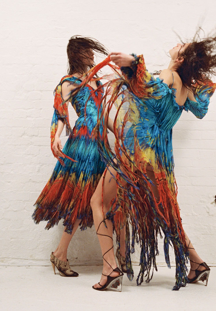 (Left) SILK KNEE LENGTH PLEATED FEATHER PRINT DRESS WORN WITH HORN HEEL FLAME MOTIF SLING BACK SHOE (Right) OFF THE SHOULDER FEATHER PRINT DRESS WITH HANDMADE FRINGE WORN WITH BLACK PYTHON LACE UP SANDAL w/ ENCASED BUTTERFLY PERSPEX HEEL Alexander McQueen S/S 2003 RTW ‘IRERE’. Photography by Hazel Gaskin