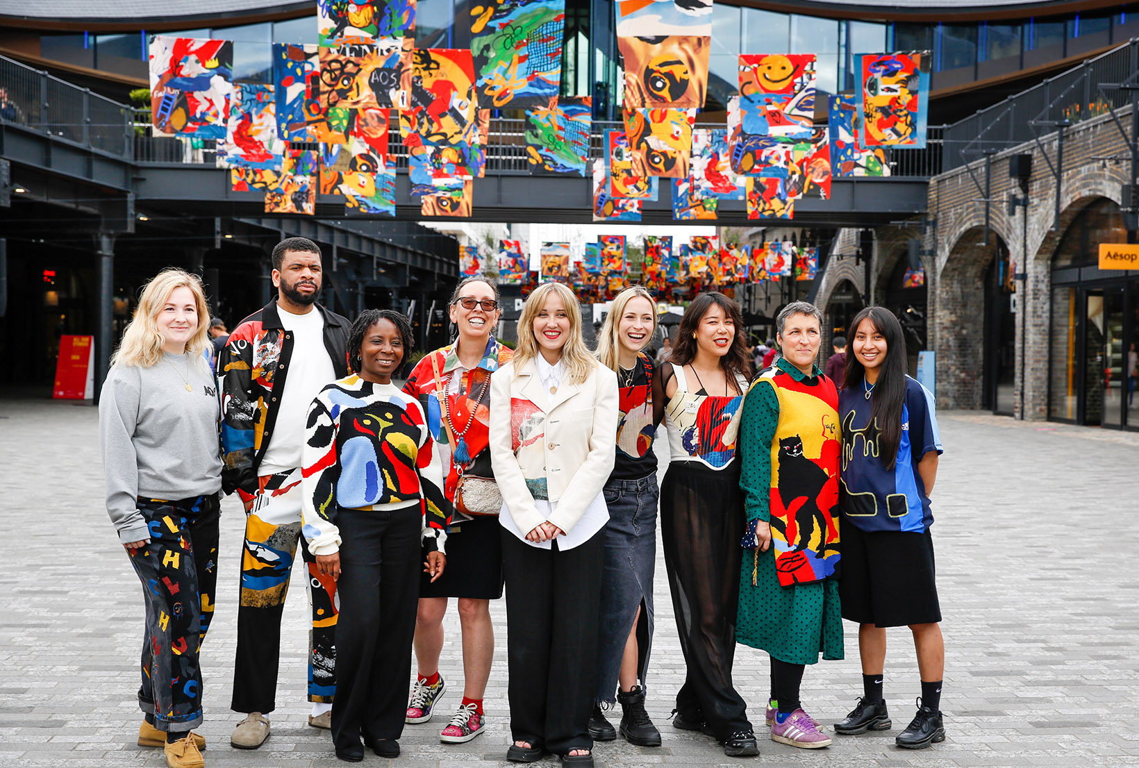 Image of Bethany Williams with members of The Magpie Trust, backed by the multicoloured flags.