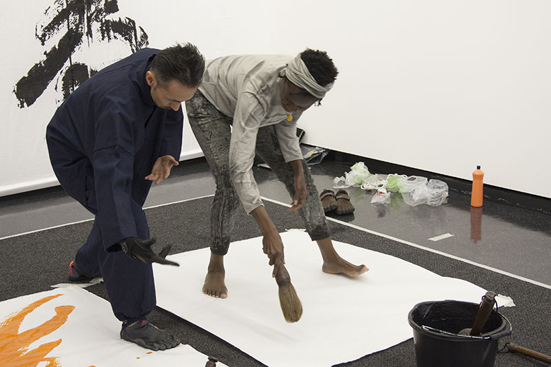 A female MA student practicing the hand and body movement of a calligraphy word next to Japanese artist Houran Yokoyama