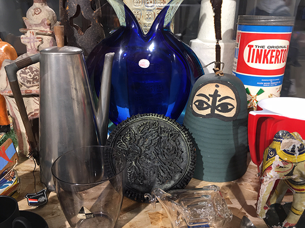 A collection of objects including a silver coffee pot, a blue vase and a wooden woman