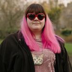 Portrait shot of Kat wearing sunglasses with pink hair